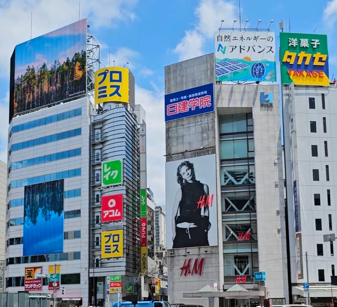 Billboards and stacked shopfront signs climbing the side of a Tokyo high-rise on a clear day